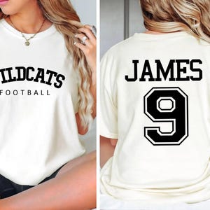 May include: White t-shirt with black text that says "Wildcats Football" on the front and "JAMES 9" on the back.