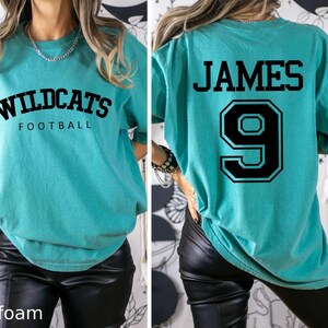 May include: A turquoise blue t-shirt with the text "Wildcats Football" on the front and the text "JAMES 9" on the back.