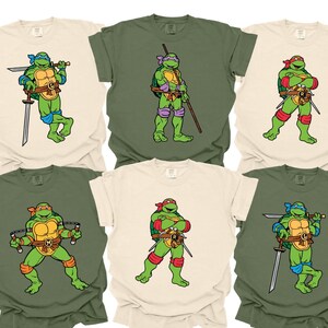 May include: A collection of six short-sleeve t-shirts in cream and olive green colors. Each shirt features a graphic illustration of a Teenage Mutant Ninja Turtle character, including Leonardo with blue gear, Donatello with purple, Raphael with red, and Michelangelo with orange accessories.