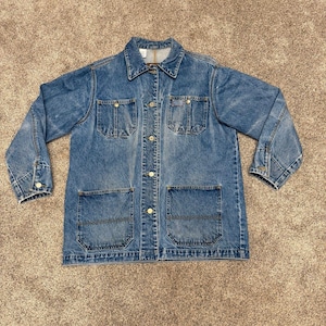 May include: A blue denim jacket featuring a collared neckline, long sleeves with buttoned cuffs, and a front button closure. The garment includes two chest pockets with buttoned flaps and two large lower patch pockets, all in a medium wash finish.