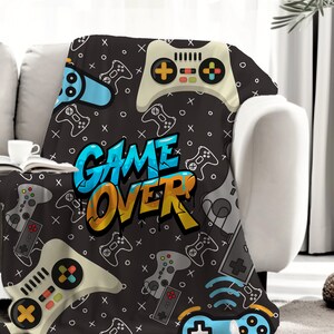 May include: A black and gray throw blanket with a repeating pattern of video game controllers and the words "GAME OVER" in colorful graffiti-style lettering.