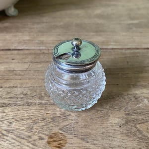 May include: A clear glass jar with a silver lid and a small spout. The jar has a diamond pattern and is sitting on a wooden surface.