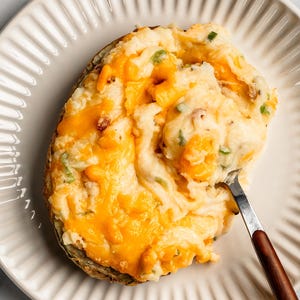 May include: A baked potato topped with melted cheese, chives, and a fork.