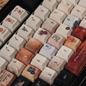 May include: A mechanical keyboard featuring custom keycaps with a vintage aesthetic. The keys display various letters, numbers, and thematic illustrations, including a long spacebar with the text My name is Sherlock Holmes, it is my business to know what other people do not know.