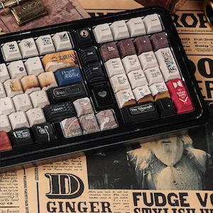 May include: A black mechanical keyboard featuring custom keycaps with Sherlock Holmes-themed designs, including text like 221B Baker Street, The Telegraph, and various book titles. The keys display vintage-style illustrations, maps, and symbols.