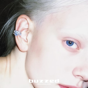 May include: A close-up of a person's face with a blue-eyed gaze and a silver ear cuff. The ear cuff has a cluster of small, light blue stones. The word "buzzed" is printed in white block letters at the bottom.