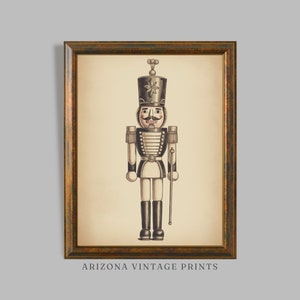 May include: A vintage illustration of a black and white toy soldier nutcracker with a red and white hat and a mustache. The nutcracker is holding a stick in its right hand. The illustration is framed in a brown frame with a gold trim.