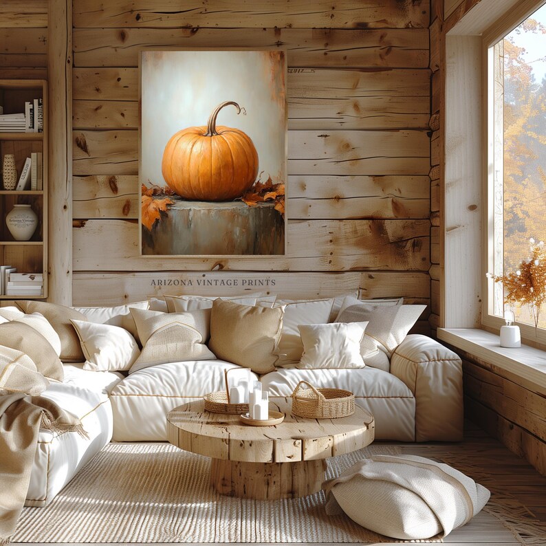 May include: A painting of a single orange pumpkin with fall leaves on a stone surface. The painting is framed and hanging on a wooden wall in a living room setting.