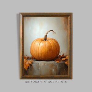 May include: A painting of a single orange pumpkin with a brown stem, sitting on a gray stone surface with brown leaves around it. The painting is framed in a gold frame.