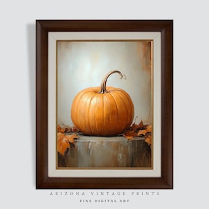 May include: A framed painting of a single orange pumpkin with a stem, sitting on a textured surface with brown leaves. The background is a light beige color.