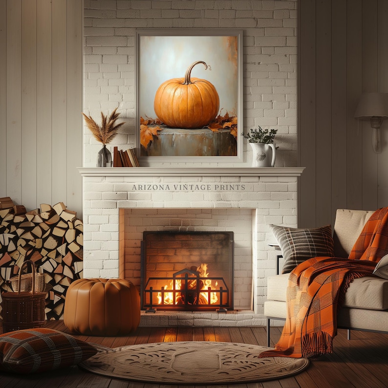 May include: A painting of a large orange pumpkin on a white background with fall leaves. The painting is framed and hanging above a fireplace with a fire burning inside. The fireplace is in a room with a white brick wall and a brown leather ottoman.