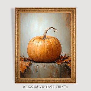 May include: A painting of a single orange pumpkin with a brown stem, sitting on a gray surface with brown leaves scattered around it. The painting is framed in a gold frame.