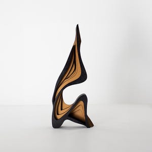 May include: Abstract wooden sculpture with a layered design. The sculpture features a black exterior with exposed tan-colored layers, creating a unique and modern aesthetic. The piece stands upright, showcasing a flowing, organic form.