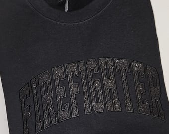 May include: Black sweatshirt with a black glitter-like "FIREFIGHTER" text in an arched design.