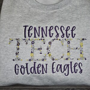 May include: Gray sweatshirt with purple embroidery that reads "Tennessee Tech Golden Eagles". The word "Tech" is surrounded by a floral design.
