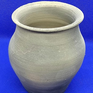 May include: A simple, unglazed, earthenware pot with a rounded body and a wide, slightly flared opening. The pot is a light brown colour and has a rough, textured surface.