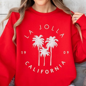 May include: Red sweatshirt with a white graphic of palm trees and the text "LA JOLLA 19 09 CALIFORNIA".