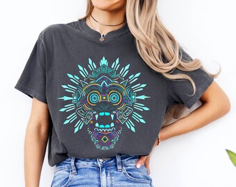 May include: A woman wearing a dark gray t-shirt with a blue and purple graphic of a stylized face. The graphic has a geometric design with a large mouth and eyes. The woman is wearing blue jeans with distressed details.