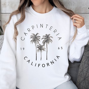 May include: White sweatshirt with a black circle graphic featuring palm trees and the text "Carpinteria 1965 California".