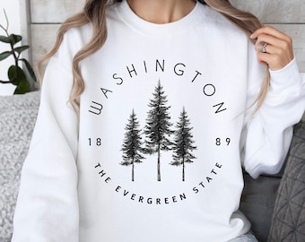 May include: White sweatshirt with a black graphic print of three evergreen trees in a circle. The text "WASHINGTON 1889 THE EVERGREEN STATE" is printed around the trees.