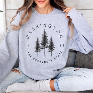 May include: A gray sweatshirt with a black graphic design featuring the words "WASHINGTON THE EVERGREEN STATE" and the numbers "1889" around a circle with three pine trees inside.