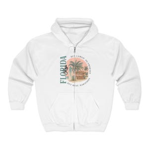 May include: White zip-up hoodie featuring a graphic of a beach scene with palm trees, a surfboard, and the text "Florida Keys Marathon". The design is in shades of blue, green, and orange.