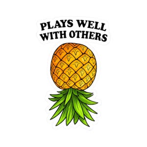 May include: A sticker with a cartoon pineapple design. The pineapple is yellow with green leaves and the text "PLAYS WELL WITH OTHERS" in black. The sticker is set against a white background.