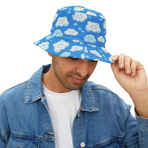 May include: A blue bucket hat with a white smiling cloud pattern. The hat is made of a soft, comfortable material and has a wide brim.