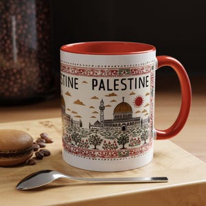 Peut inclure: Une tasse en céramique blanche avec un bord et une poignée rouges. La tasse présente une illustration colorée du Dôme du Rocher à Jérusalem, avec les mots "Palestine" imprimés sur le côté.