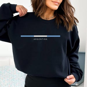 May include: Black sweatshirt with a blue and white stripe and the word "ARGENTINA" printed on the front.