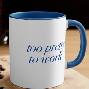 May include: White ceramic mug with a blue rim and handle. The mug has the text "too pretty to work" printed in blue on the front.