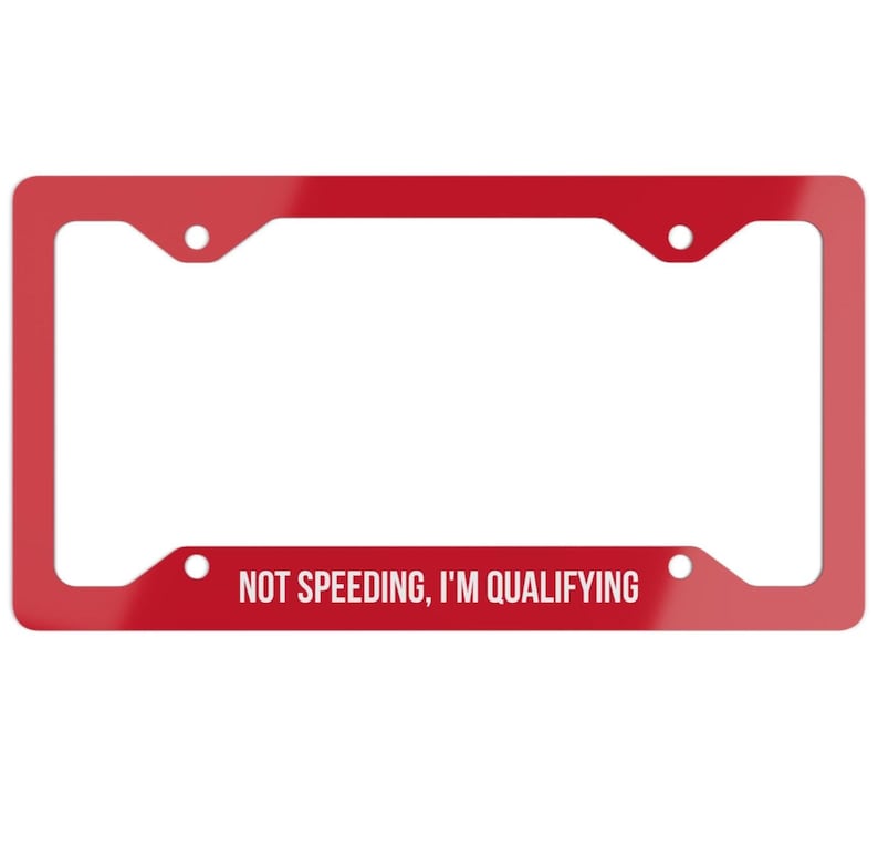 Op de afbeelding: Een rode kentekenplaathouder met de witte tekst "NOT SPEEDING, I'M QUALIFYING". De houder heeft vier montagegaten en een glanzende afwerking. Een leuk accessoire voor elk voertuig.