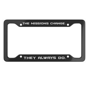 May include: Black license plate frame with the text "THE MISSIONS CHANGE. THEY ALWAYS DO." in white lettering. The frame has a rectangular shape with rounded corners and mounting holes.