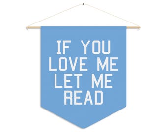 Op de afbeelding: Een lichtblauwe banner met de tekst "IF YOU LOVE ME LET ME READ" in witte blokletters. De banner is opgehangen aan een houten stok met een wit touwtje.