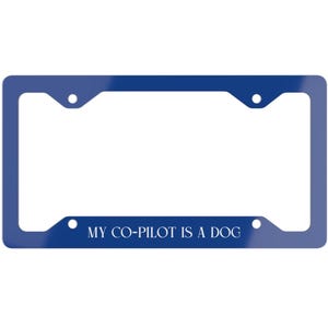 May include: A blue license plate frame with the white text "MY CO-PILOT IS A DOG". The frame has a glossy finish and is designed for a standard-sized license plate. It features four mounting holes for attachment.