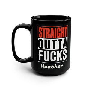 Puede incluir: Taza de cerámica negra con el texto "STRAIGHT OUTTA FUCKS" en letras de bloque rojas y blancas. El nombre "Heather" está impreso en blanco debajo. La taza tiene un asa grande.