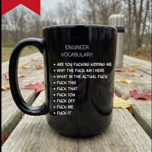 Puede incluir: Una taza de cerámica negra con texto blanco que dice ENGINEER VOCABULARY: seguido de una lista con viñetas de frases que incluyen ARE YOU FUCKING KIDDING ME, WHY THE FUCK AM I HERE, WHAT IN THE ACTUAL FUCK, FUCK THIS, FUCK THAT, FUCK YOU, FUCK OFF, FUCK ME, FUCK IT.