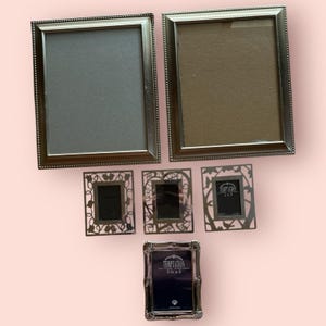 May include: Two large rectangular silver-toned picture frames with beaded edges, three smaller rectangular silver-toned frames with intricate cut-out floral patterns, and one ornate silver-toned frame labeled Temptation 3.5 x 5 inches.