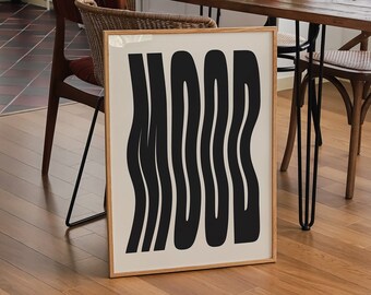 May include: A framed art print with the word "MOOD" in black, wavy letters. The print is displayed on a wooden floor, leaning against a wall. The room has a dining table with a plant, apple, and wine bottle.