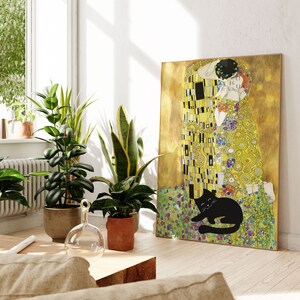 May include: A framed canvas print of Gustav Klimt's "The Kiss" with a black cat illustration at the bottom. The artwork features gold, yellow, and colorful floral patterns. The print is displayed in a well-lit room with potted plants.