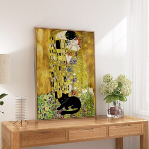 May include: A framed print of Gustav Klimt's "The Kiss" with a black cat illustration. The artwork features gold, yellow, and colorful accents. The print is displayed on a wooden console table, with a lamp and flowers.