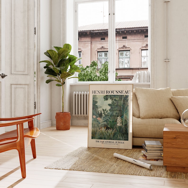 May include: A framed poster with a jungle scene and the text "Henri Rousseau, The Equatorial Jungle, The National Gallery of Art, 1930". The poster is hanging on a white wall in a living room with a beige couch, a wooden chair, and a potted plant.