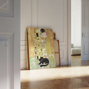 May include: A large canvas print of Gustav Klimt's "The Kiss" with a black cat illustration in the foreground. The artwork features gold, yellow, and black geometric patterns. Additional blank canvases lean against the wall.