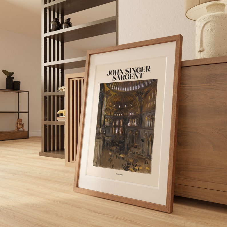 May include: A framed art print featuring a watercolor painting of a cathedral interior, with the text "JOHN SINGER SARGENT" at the top. The print is in a light brown wooden frame, leaning against a wooden cabinet.