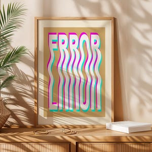 May include: A framed print featuring the words "ERROR LIMIT" in a layered, wavy design. The text is white, pink, and teal on a tan background. The artwork is displayed on a wooden surface.
