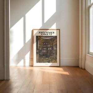 May include: A framed art print featuring a watercolor painting of a cathedral interior. The print is in a light brown wooden frame and leans against a white wall. The text "JOHN SINGER SARGENT" is at the top of the print.