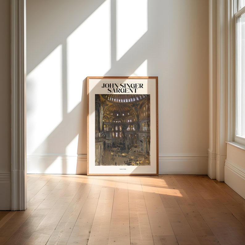 May include: A framed art print featuring a watercolor painting of a cathedral interior. The print is in a light brown wooden frame and leans against a white wall. The text "JOHN SINGER SARGENT" is at the top of the print.