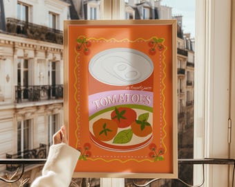 Op de afbeelding: Een ingelijste kunstprint met een gestileerde illustratie van een tomatenblik. Het kunstwerk heeft een levendige oranje achtergrond met een decoratieve rand van kersen. Het blik is afgebeeld met een zilveren deksel en het woord "TOMATEN" in roze.