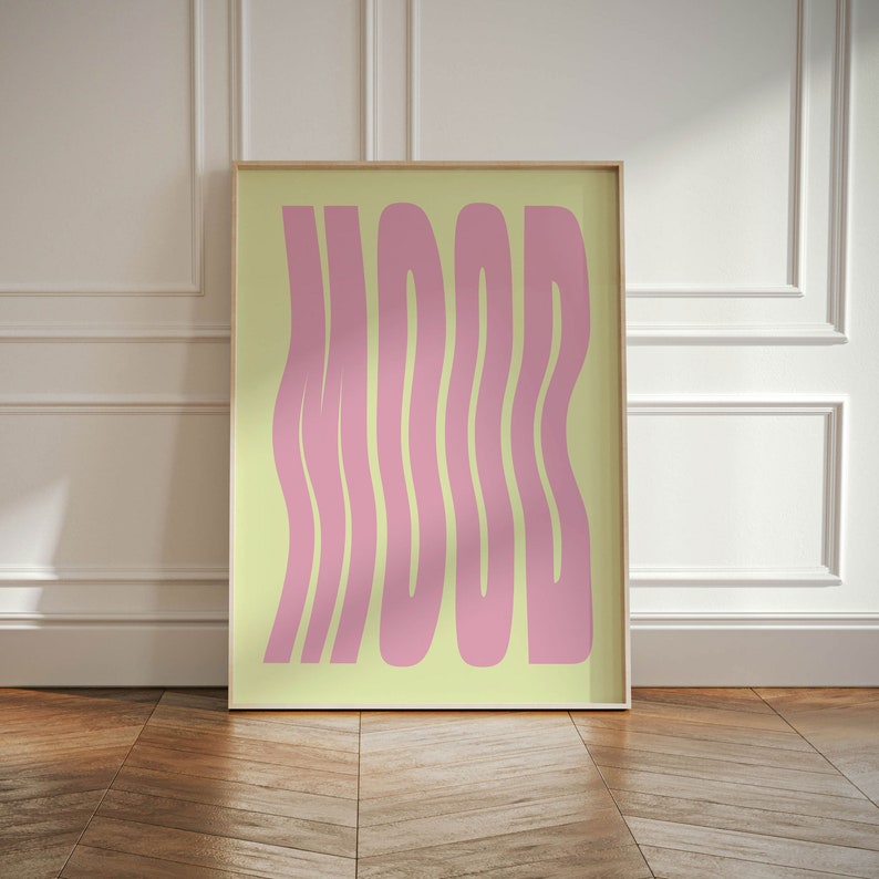 May include: A framed print with a yellow background and pink text that reads "MOOD". The text is stylized with wavy lines.