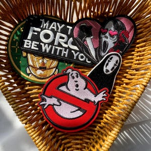 May include: A collection of embroidered patches featuring pop culture references. Includes a Star Wars patch with "MAY THE FORCE BE WITH YOU", a Ghostbusters patch, a Scream patch, and a Spirited Away patch. The patches are displayed in a heart-shaped wicker basket.